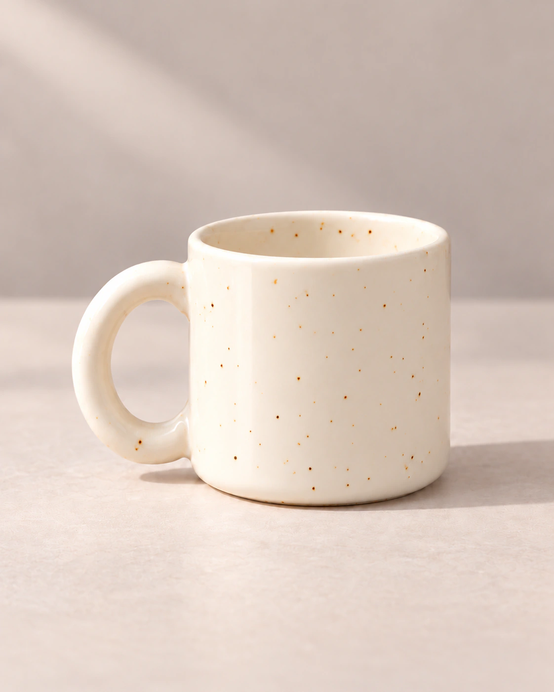 Ivory speckled stoneware mug on a light neutral surface.